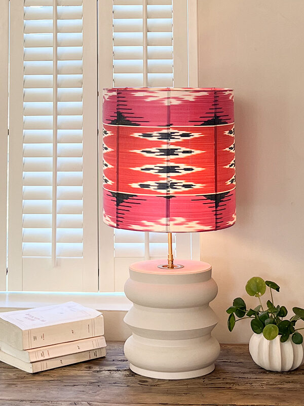 Lampe de chevet originale Rêve en Rose allumée, avec abat-jour en soie ikat rose, rouge et bleu, sur pied en faïence blanche mate