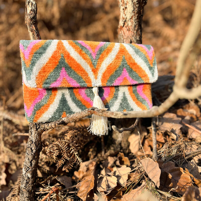 Pochette en velours BOHO rose orangé posée sur des feuilles en forêt à l’automne