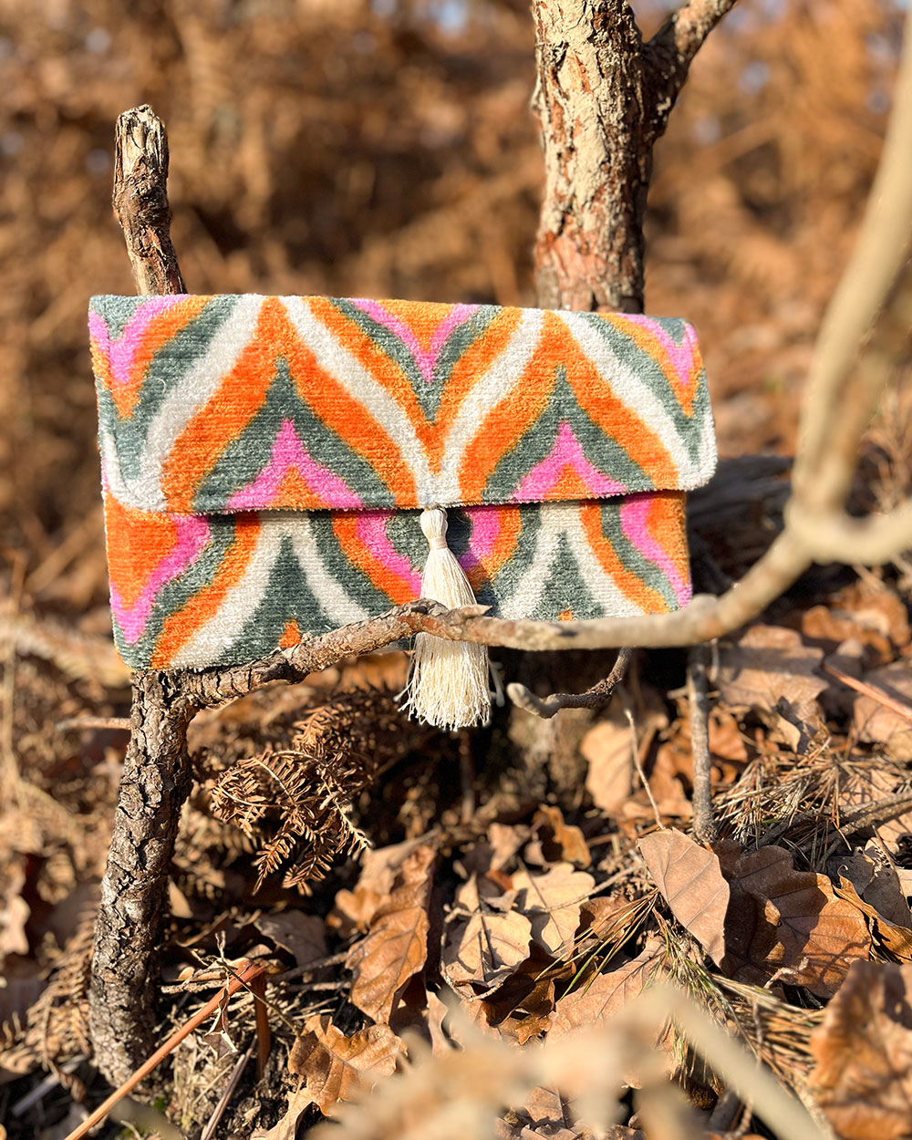 Pochette en velours BOHO rose orangé posée sur des feuilles en forêt à l’automne