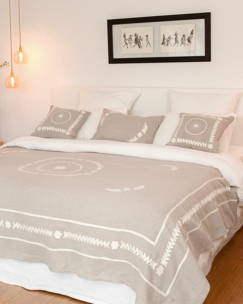 Coussin brodé en lin ficelle Navli posé sur couvre-lit assorti.