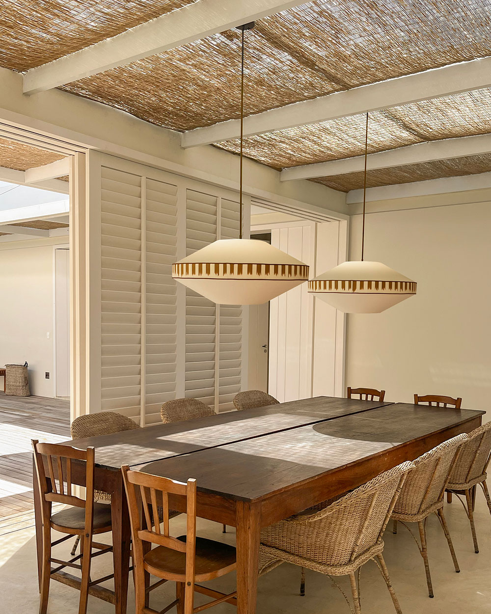 Suspensions lumineuses au-dessus d’une table en bois dans une maison d’été baignée de lumière